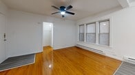 Located at 5957-5973 W Madison St in Chicago, IL, this single-floor unit offers an efficient and functional layout across its compact footprint. The combined kitchen and living area forms the heart of the space, where two distinct flooring materials meet — warm, classic hardwood in the living zone transitions to durable vinyl plank in the kitchen area. The kitchen is outfitted with honey-toned wood cabinetry, a stainless steel range, a black refrigerator, a single-basin sink, and a dedicated electrical panel, all illuminated by recessed ceiling lighting. The living area benefits from natural light provided by double windows fitted with blinds, and is equipped with a ceiling fan for additional air circulation. A baseboard heating system runs along the perimeter walls, ensuring year-round comfort. The space includes a closet, visible from the living area, providing practical storage. The all-white bathroom features a vanity with a medicine cabinet, a bathtub with a shower, and a window for ventilation. Clean white walls throughout the unit create a bright, neutral backdrop that maximizes the sense of space within this efficiently designed Chicago residence.