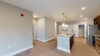 Located at 4525 Croquet Dr in Wilmington, NC, this single-floor residence showcases a clean, contemporary design characterized by neutral gray walls, white trim, and a cohesive color palette carried throughout. The open-concept kitchen and living area serves as the heart of the home, featuring light wood-look flooring that extends seamlessly across the main living spaces. The kitchen is appointed with dark cabinetry, stainless steel appliances including a refrigerator with ice maker, electric range, and microwave, complemented by granite countertops and a center island with a built-in sink. Pendant lighting above the island adds a refined finishing touch, while recessed lighting illuminates the broader space. An in-unit laundry area is conveniently integrated nearby. The living area opens to the outdoors through glass French doors, inviting natural light. The bedrooms feature plush carpet flooring and windows with blinds that provide natural light and outdoor views. The bathrooms are well-appointed, offering a dual-sink vanity with granite countertops and dark cabinetry in one bath, alongside a tub-shower combination. The overall layout is functional and thoughtfully designed for comfortable everyday living.