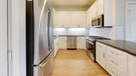 This well-appointed single-floor residence offers a clean, modern aesthetic throughout, with light-toned hardwood flooring and a neutral color palette that creates a warm, inviting ambiance. The open-concept layout seamlessly connects the kitchen and living area, maximizing the sense of space and encouraging easy flow between rooms. The kitchen is thoughtfully designed with white shaker cabinetry, dark countertops, a white tile backsplash, and a full suite of stainless steel appliances including a gas range, dishwasher, microwave, and refrigerator. A central island provides additional workspace and casual dining options. Crown molding accents the living area, which features a fireplace as a focal point and access to a private balcony where natural light pours in through a sliding glass door. Multiple bedrooms offer generous proportions, each filled with natural light from large windows that frame views of surrounding greenery. The bathrooms are finished with white cabinetry, dark countertops, and full tub-shower combinations. One bathroom includes a backlit vanity mirror, adding a refined touch. Throughout the residence, recessed lighting and clean white walls contribute to a bright, move-in-ready environment.