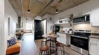 Located at 708 22nd St in Greeley, Colorado, this one-bedroom, one-bathroom unit delivers an industrial-chic aesthetic with thoughtful modern finishes. The exposed concrete ceiling and track lighting run throughout, creating a bold, loft-inspired character that defines the space.

The kitchen is efficiently designed with white cabinetry, open shelving, dark stone countertops, and stainless steel appliances including a range, microwave, and refrigerator. A compact round bistro table with industrial-style stools provides a casual dining area just steps from the kitchen.

Hardwood-style flooring extends through the main living and kitchen areas, transitioning to plush carpet in the generously sized bedroom. The bedroom features a large window that allows natural light to fill the room, complemented by a sliding closet with an in-unit washer and dryer. Exposed concrete ceilings continue here, reinforcing the cohesive industrial design language.

The bathroom is clean and contemporary, featuring a trough-style sink, modern fixtures with matte black accents, and wood-tone flooring. A long corridor connects all areas of the unit, maximizing functionality within the compact footprint.

Overall, the space blends raw architectural elements with modern comfort, making it a well-appointed urban residence in Greeley, CO.