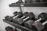 This fitness room offers a comprehensive workout environment designed to support a wide range of exercise routines. The space is anchored by vaulted ceilings fitted with dual ceiling fans, creating an open, airy atmosphere that keeps the room comfortable during workouts. Durable speckled rubber flooring runs throughout, providing both safety and easy maintenance.

The cardio zone lines the windowed wall, where multiple treadmills, an elliptical trainer, and a stationary bike are arranged to take advantage of natural light filtering through slatted blinds. A dedicated strength training area features a multi-station cable machine, a full rack of dumbbells in graduated weights, and adjustable benches for versatile resistance training. A collection of stability and medicine balls adds options for functional fitness and core work.

A wall-mounted flat-screen television is positioned for easy viewing from the cardio equipment, enhancing the workout experience. Motivational artwork and framed prints decorate the bright white walls, contributing to an energizing ambiance. A hallway connects to a secondary area equipped with a water fountain and bottle-filling station, ensuring hydration is always within reach. Multiple entry and exit points, including a glass-panel exterior door, provide convenient access throughout the space.
