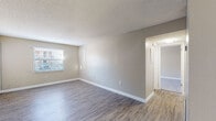 This single-floor residence offers a thoughtfully designed layout with a clean, neutral aesthetic throughout. The open living area is finished with durable luxury vinyl plank flooring in a warm gray tone, complemented by crisp white baseboards and soft beige walls. Natural light filters in through blinded windows, creating a bright and welcoming atmosphere. A sliding glass door leads to an outdoor area, further enhancing the sense of openness in the main living space.

The kitchen is a standout feature, boasting granite countertops with rich veining, white shaker-style cabinetry with modern bar-pull hardware, and a sleek gray subway tile backsplash. Stainless steel appliances, including a dishwasher and electric range with overhead ventilation, complete the functional and stylish cooking space. A window above the sink adds natural light to the galley-style layout.

The bedrooms are carpeted for comfort and each features a window with exterior views, providing ample natural light. The neutral tones carry throughout, maintaining a cohesive and serene feel. The bathroom includes a full-size soaking tub with an overhead shower, finished in clean white surrounds. Textured ceilings are present throughout the home, adding a subtle architectural detail to each room.