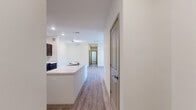 This thoughtfully designed residence spans two floors and offers three bedrooms and three full bathrooms. The open-concept kitchen and living area serves as the heart of the home, featuring light wood-look luxury vinyl plank flooring, recessed lighting, and a large kitchen island with a white quartz-style countertop and an integrated sink. The kitchen is equipped with dark espresso-toned cabinetry, black appliances including a gas range, microwave, and refrigerator, creating a striking contrast against the bright white walls and countertops.

A central hallway connects the main living areas to the bedrooms, which feature plush carpeting and ample natural light through horizontal-blind-fitted windows overlooking the surrounding community. Each bedroom provides generous proportions, with the primary bedroom offering a dedicated walk-in closet fitted with wire shelving for organized storage.

The three bathrooms are finished consistently with wood-look flooring, dark vanity cabinetry, and white countertops. At least one bathroom features a full soaking tub with a shower surround. A private balcony accessible from the unit provides open views of the community grounds, parking areas, and neighboring buildings under expansive skies.