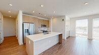 Located at 150–198 W Jewell Ave in Denver, Colorado, this single-floor unit showcases a clean, modern design characterized by neutral tones, quality finishes, and an efficient layout. The open-concept living and kitchen area serves as the centerpiece of the space, anchored by a substantial island with a white quartz countertop and an integrated sink. Light wood-grain cabinetry lines the kitchen walls, complemented by a tile backsplash and a full suite of stainless steel appliances, including a side-by-side refrigerator, electric range, and microwave. Recessed lighting and wood-look flooring extend throughout the main living area, which transitions seamlessly into a bright sitting or dining space featuring built-in shelving, lower cabinetry, and expansive floor-to-ceiling windows that flood the room with natural light and offer open city views. The bedrooms are carpeted and well-lit by large windows. The bathroom is a standout feature, finished with large-format marble-look tile flooring and wall surround, a floating wood vanity with a white basin, and brass fixtures. A walk-in closet with organized shelving connects directly to the bathroom, adding practical functionality to the refined aesthetic throughout.