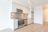 Located at 205 Queen St E in Brampton, Ontario, this thoughtfully designed one-bedroom, one-bathroom unit offers a clean, modern aesthetic throughout its efficiently laid-out single floor. Light wood-tone flooring flows continuously across every room, creating a cohesive and airy feel.

The kitchen is a standout feature, showcasing flat-panel white cabinetry extending to the ceiling for ample storage, a neutral quartz-style countertop, a grey subway tile backsplash, and a full suite of stainless steel appliances including a range, over-the-range microwave, dishwasher, and refrigerator. Track lighting overhead adds a contemporary finishing touch.

The bedroom is bright and calm, benefiting from a large window that invites natural light, with clean white walls and the same warm flooring underfoot. It is complemented by a dedicated walk-in closet with built-in rod and shelf storage, providing practical organization space.

The bathroom is finished in a minimalist style with wood-look flooring, a tiled shower surround, a floating vanity with a light stone-top, and matte black hardware accents including a towel bar and toilet paper holder — details that add a refined, modern character.

Throughout, the unit features crisp white walls, recessed lighting, and a neutral palette that creates a clean, move-in-ready environment suitable for a variety of lifestyles.