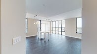 Located at 33 Monroe St in the heart of Rockville, MD, this contemporary single-floor residence offers a thoughtfully designed open layout with modern finishes throughout. The expansive living and dining area is a standout, featuring dark hardwood flooring, track lighting, and dramatic floor-to-ceiling windows that flood the space with natural light and frame views of the surrounding cityscape. A structural column adds an architectural accent, while vertical blinds provide adjustable privacy.

The kitchen is well-appointed with stainless steel appliances — including a range, dishwasher, microwave, and refrigerator — complemented by stone countertops, a classic subway tile backsplash, and a mix of white upper and wood-toned lower cabinetry. The open entry area connects seamlessly to the main living space and kitchen.

The bedrooms feature plush carpeting and generous windows with horizontal blinds, offering views of the Rockville streetscape and ample natural light. Closet space is provided with paneled doors. The bathrooms are clean and modern, each featuring light tile flooring, a soaking tub with shower combination, chrome fixtures, a curved shower rod, and a wood-accented vanity with stone countertop. The overall ambiance is bright, neutral, and move-in ready.