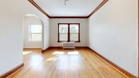 This single-floor unit showcases a thoughtful layout with distinctive vintage character throughout. Warm-toned hardwood floors run continuously across the living areas and bedrooms, reflecting natural light and adding a sense of warmth and cohesion to the space.

The living room is a standout area, featuring rich dark wood crown molding and baseboards, a ceiling fan, and a classic white cast-iron radiator positioned beneath a pair of windows that frame views of mature trees. A graceful arched doorway connects the living room to the adjoining spaces, lending an elegant architectural detail to the open flow of the floor plan.

The bedrooms are well-proportioned and bright, each benefiting from multiple windows with tree-lined views, hardwood floors, and cast-iron radiators, providing both natural light and traditional heating character.

The galley-style kitchen is efficiently arranged, featuring white cabinetry with ample storage, white appliances including a range and refrigerator, and neutral tile flooring that contrasts cleanly with the wood floors elsewhere.

The bathroom maintains the home's classic aesthetic, complete with a soaking tub, pedestal sink, and a window that allows natural light to filter in. Throughout the unit, the combination of period details and bright, neutral walls creates a timeless and inviting ambiance.
