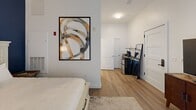 Located in Woburn, MA, this efficiently designed one-bedroom, one-bathroom unit offers a well-organized single-floor layout that maximizes every square foot. The interior features light wood-toned flooring throughout, crisp white walls, and clean panel-style doors with matte black hardware, lending a modern and cohesive aesthetic.

The generously proportioned bedroom serves as the heart of the unit, accommodating a full sleeping area with room to spare. Sheer white curtains frame a sliding glass door that invites natural light and provides outdoor access, creating an airy, open feel. A dedicated living area adjacent to the bedroom is anchored by a classic entryway door and offers flexible space for a media setup or lounge area.

The bathroom is finished in a neutral, spa-like palette with large-format tile flooring and an all-white walk-in shower stall equipped with brushed nickel fixtures, including a handheld showerhead. Light wood cabinetry provides practical storage, while the overall design maintains a clean, minimalist character.

Throughout the unit, thoughtful details such as recessed lighting, a smart thermostat panel, and well-placed wall art opportunities contribute to a polished, move-in-ready atmosphere suited for those seeking a streamlined and functional living space in the Woburn area.