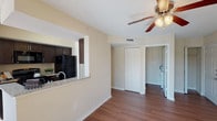 This single-floor residence offers a thoughtfully designed open-concept layout that seamlessly connects the main living areas. Rich hardwood-style flooring runs throughout, complementing the warm, neutral tones of the walls and creating a cohesive, inviting atmosphere.

The kitchen is outfitted with dark espresso cabinetry, granite-look countertops, and black appliances including a refrigerator, electric range, and over-the-range microwave. A pass-through counter opens directly to the living area, making the space ideal for entertaining.

The living room is bright and airy, benefiting from abundant natural light streaming through large windows and a sliding glass door that opens to a private balcony with outdoor views. A ceiling fan with integrated lighting adds both comfort and function to the space.

The bedroom is generously sized, featuring a window with natural light and hardwood-style flooring. It is accompanied by a spacious walk-in closet equipped with multiple wire shelving units and hanging rods, offering excellent storage capacity.

The bathroom is finished with a dark vanity cabinet, granite-look countertop, a large mirror with overhead lighting, and a shower-tub combination. A louvered closet door in the hallway provides additional storage convenience. The textured ceilings throughout add a classic residential character to the overall design.