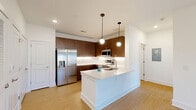 This thoughtfully designed one-bedroom, one-bathroom residence in Hendersonville, NC offers a clean, modern aesthetic with consistent light wood-tone flooring and crisp white walls throughout. The open-concept kitchen and living area serves as the heart of the home, featuring a sleek island with a white quartz countertop and undermount sink, rich dark walnut-toned cabinetry, stainless steel appliances including a French door refrigerator, electric range, and over-the-range microwave, plus a textured tile backsplash with under-cabinet lighting. The living area is bathed in natural light from French doors that open to a private balcony, and a ceiling fan adds comfort overhead. The bedroom is a serene retreat with a window offering outdoor views, a ceiling fan, and direct access to a spacious walk-in closet outfitted with built-in shelving and dual hanging rods. A second closet provides additional storage. The bathroom features a walnut-toned vanity with a white countertop, a large framed mirror, and a full soaking tub with shower. Additional conveniences include a dedicated laundry area and a pantry, rounding out a well-appointed and efficiently organized living space.