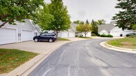 Located on Crystal Bay Court SW in Rochester, Minnesota, this single-floor residence offers a comfortable and practical layout within a well-established neighborhood. The exterior showcases classic light gray siding with clean architectural lines, accented by a distinctive arched window detail above the attached two-car garage. The wide concrete driveway provides ample parking and leads directly to the garage, offering convenient and covered vehicle storage. The home is set within a landscaped lot featuring mature evergreen and deciduous trees that lend a sense of privacy and natural charm. The surrounding community is characterized by similarly styled homes, a shared paved roadway, and additional open parking areas lined with towering conifers — contributing to a serene, park-like atmosphere. The gently rolling green lawn enhances the curb appeal of the property, reflecting a well-kept residential environment. Situated on a quiet cul-de-sac-style street, the location offers a peaceful setting while remaining part of an established Rochester neighborhood, making it a functional and inviting place to call home.