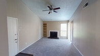 Located at 5229 Hunters Ridge Rd in Fort Worth, TX, this single-story home offers a well-organized layout with distinct living, kitchen, sleeping, and bathroom areas. The living room serves as the focal point of the home, showcasing vaulted ceilings with a textured finish and a ceiling fan with light fixture. A wood-burning fireplace with a white surround and dark hearth anchors one wall, while an adjacent built-in shelving unit provides convenient display and storage space. Natural light filters in through a window flanking the fireplace, and the room is finished with wall-to-wall carpet throughout. The galley-style kitchen features dark espresso cabinetry on both sides, granite-look countertops, a black electric range, a sink, and wood-look flooring, creating a functional and efficient cooking space. The hallway connects the main living areas to the bedroom and bathroom. The bedroom is a generously sized, carpeted room with neutral walls and a textured ceiling. The full bathroom includes a tub-shower combination with white tile surround, a toilet, a vanity with granite-look countertop, and wood-look flooring. The overall ambiance of the home is neutral and move-in ready.
