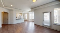 This well-designed single-floor residence offers a bright, open-concept layout that seamlessly connects the living, dining, and kitchen areas. Rich hardwood-style flooring flows throughout the main living spaces, complemented by an abundance of natural light streaming through multiple windows fitted with blinds. A ceiling fan overhead adds both function and style to the living area, which also features a private exterior door entry.

The kitchen is a standout feature, showcasing crisp white cabinetry extending to the ceiling for ample storage, striking dark hexagonal mosaic tile backsplash, granite-look countertops, and a full suite of stainless steel appliances including a French door refrigerator, electric range, built-in microwave, and a modern sink with a gooseneck faucet. A peninsula counter provides additional workspace and casual seating.

The bedrooms offer plush carpeting, ceiling fans, and generous windows that bring in natural light. The primary bathroom features a double-sink vanity with dark countertops, wood-style flooring, and a glass-enclosed walk-in shower with elegant linear tile surround. A second bathroom includes a tiled shower-tub combination and hardwood-style flooring, providing comfortable accommodations for guests.
