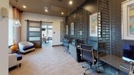 This thoughtfully designed single-floor space blends contemporary style with functional amenities across several distinct zones. The business center is defined by bold, dark metal lattice partitions that create semi-private workstations equipped with ergonomic seating and built-in desks, lending an industrial-modern character to the area. Stone-look tile flooring runs throughout, tying the spaces together with a cohesive, upscale aesthetic.

A standout feature is the conference or dining area, which boasts soaring ceilings and an impressive bank of floor-to-ceiling windows that frame views of surrounding natural landscape. A live-edge wood table anchors the room, paired with eclectic upholstered seating in a mix of geometric patterns and neutral tones. A bold teal accent wall and an oversized drum pendant light add drama and warmth to this gathering space.

A cozy lounge nook offers a more intimate retreat, furnished with curved barrel chairs, a decorative side table, and a geometric pendant light. Vibrant chevron-patterned drapery and a sliding barn door add texture and personality to the space.

Connecting hallways are accented with framed artwork and bold patterned wall coverings, while recessed lighting throughout ensures a well-lit, welcoming atmosphere. Overall, the space presents a dynamic and polished environment ideal for work, collaboration, and relaxation.