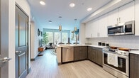Located at 9 City Blvd in Nashville, TN, this thoughtfully designed one-bedroom, one-bathroom residence offers a contemporary living experience with efficient use of space throughout. The open-concept kitchen and living area serves as the heart of the home, where the kitchen features a two-tone cabinet design pairing crisp white upper cabinets with dark wood-grain lower cabinets, white quartz countertops, a peninsula with pendant lighting, and a full suite of stainless steel appliances including a range, over-the-range microwave, dishwasher, and refrigerator. Light wood-style flooring flows seamlessly through the main living area, enhancing the bright, airy ambiance created by large windows that invite abundant natural light and views of surrounding greenery. The living room offers a comfortable, modern atmosphere. The bedroom features plush carpeting, a ceiling fan, and a generous window with elegant drape treatments, providing a calm and restful retreat. The bathroom is finished with wood-grain cabinetry, a white quartz vanity, a large framed mirror, and a glass-enclosed shower, all set on light wood-style flooring. A hallway connects all rooms efficiently, completing this well-appointed Nashville residence.