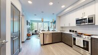 Located at 9 City Blvd in Nashville, TN, this thoughtfully designed one-bedroom, one-bathroom residence offers a contemporary living experience with efficient use of space throughout. The open-concept kitchen and living area serves as the heart of the home, where the kitchen features a two-tone cabinet design pairing crisp white upper cabinets with dark wood-grain lower cabinets, white quartz countertops, a peninsula with pendant lighting, and a full suite of stainless steel appliances including a range, over-the-range microwave, dishwasher, and refrigerator. Light wood-style flooring flows seamlessly through the main living area, enhancing the bright, airy ambiance created by large windows that invite abundant natural light and views of surrounding greenery. The living room offers a comfortable, modern atmosphere. The bedroom features plush carpeting, a ceiling fan, and a generous window with elegant drape treatments, providing a calm and restful retreat. The bathroom is finished with wood-grain cabinetry, a white quartz vanity, a large framed mirror, and a glass-enclosed shower, all set on light wood-style flooring. A hallway connects all rooms efficiently, completing this well-appointed Nashville residence.