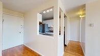 This well-appointed single-floor unit offers a thoughtful layout that balances open communal spaces with private retreats. The living area is a welcoming, light-filled space featuring warm hardwood flooring and a ceiling fan overhead. A textured ceiling adds character, while a large sliding glass door floods the room with natural light and opens to expansive outdoor views of the surrounding neighborhood — a true highlight of the space. The transition between hardwood and plush carpet delineates the living zone from a more relaxed lounging area. The galley-style kitchen is efficiently designed, featuring white cabinetry with ample upper and lower storage, dark granite-style countertops, a double stainless steel sink, a dishwasher, an electric range, and a full-size refrigerator. A distinctive pass-through window connects the kitchen to the adjacent living and dining area, enhancing the sense of openness. The bedrooms are carpeted for comfort, each finished with neutral tones and closet storage. One bedroom includes a ceiling fan and direct entry access. Throughout, the unit maintains a clean, neutral palette with white trim and walls, creating a bright, move-in-ready atmosphere that is both functional and inviting.