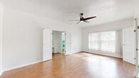 Located at 511 S Serrano Ave in the Koreatown neighborhood of Los Angeles, this single-floor unit offers a well-organized layout comprising a living room, kitchen, bathroom, hallway, closet, and entrance. The living room is a standout space, featuring warm hardwood flooring that runs throughout, crisp white walls, and a modern ceiling fan with integrated lighting. A large window dressed with vertical blinds allows generous natural light to flood the room, while a charming arched doorway adds a touch of classic architectural character. The galley-style kitchen is outfitted with white cabinetry — including glass-front upper cabinets — white tile countertops with decorative black diamond accents, a stainless steel sink, and full-size white appliances. A bold black-and-white checkered floor lends the kitchen a timeless, retro aesthetic. The bathroom is a striking nod to mid-century design, showcasing vibrant green ceramic wall tiles, hexagonal green floor tiles, a soaking bathtub, a pedestal sink, and a louvered window that provides natural ventilation and light. The overall ambiance of the unit is bright, clean, and characterized by vintage details that give it a distinctive personality within the Los Angeles rental market.