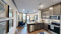 Located at 1250 S Egret Bay Blvd in League City, TX, this well-appointed one-bedroom, one-bathroom residence offers a thoughtfully designed single-floor layout with modern finishes throughout. The kitchen is a standout feature, showcasing rich dark cabinetry, granite countertops, and a full suite of stainless steel appliances including a refrigerator, range, and microwave. A peninsula with pendant lighting provides casual dining space and serves as a natural divider between the kitchen and living area, enhancing the open flow of the home. Wood-style flooring runs throughout, lending warmth and visual continuity to the space. The bedroom is generously proportioned, featuring a ceiling fan, large windows that invite natural light, and views of the landscaped exterior. It connects to a spacious walk-in closet outfitted with multi-tiered wire shelving for ample storage. The bathroom is clean and functional, offering a granite-topped vanity with dark cabinetry, a tub-shower combination, and tasteful finishes consistent with the rest of the home. A hallway connects the rooms efficiently, contributing to the unit's practical layout. The exterior features manicured greenery, flowering shrubs, and a patio with railing, providing a pleasant outdoor setting.