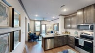 Located at 1250 S Egret Bay Blvd in League City, TX, this well-appointed one-bedroom, one-bathroom residence offers a thoughtfully designed single-floor layout with modern finishes throughout. The kitchen is a standout feature, showcasing rich dark cabinetry, granite countertops, and a full suite of stainless steel appliances including a refrigerator, range, and microwave. A peninsula with pendant lighting provides casual dining space and serves as a natural divider between the kitchen and living area, enhancing the open flow of the home. Wood-style flooring runs throughout, lending warmth and visual continuity to the space. The bedroom is generously proportioned, featuring a ceiling fan, large windows that invite natural light, and views of the landscaped exterior. It connects to a spacious walk-in closet outfitted with multi-tiered wire shelving for ample storage. The bathroom is clean and functional, offering a granite-topped vanity with dark cabinetry, a tub-shower combination, and tasteful finishes consistent with the rest of the home. A hallway connects the rooms efficiently, contributing to the unit's practical layout. The exterior features manicured greenery, flowering shrubs, and a patio with railing, providing a pleasant outdoor setting.