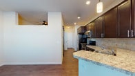This single-story residence offers a thoughtfully designed open layout that integrates the kitchen and living areas seamlessly. The kitchen serves as a central highlight, featuring rich dark cabinetry with sleek hardware, light granite countertops, and a neutral tile backsplash. Stainless steel appliances—including a range, over-the-range microwave, and dishwasher—add a modern, polished finish. A peninsula with a double stainless steel sink and pendant lighting above creates a natural divide between the kitchen and the adjacent dining and living spaces, enhancing both function and flow.

The living area is bright and open, benefiting from natural light admitted through a glass exterior door flanked by windows. A ceiling fan provides additional comfort. Wood-style flooring runs consistently throughout the main living spaces, adding warmth and visual continuity. The bedroom is a generously proportioned space with the same flooring and neutral wall tones, offering a clean, move-in ready aesthetic.

The bathroom includes dark wood vanity cabinetry with white countertops, a framed mirror, and wood-style flooring that echoes the rest of the unit. A walk-through area beyond the vanity leads to additional storage or a walk-in closet, adding practical utility to the space.