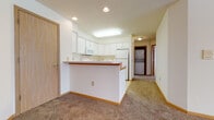 Located at 3271 W Main St in Sun Prairie, Wisconsin, this single-floor unit offers a practical and well-organized layout suited for comfortable everyday living. The open-concept living area is generously sized, featuring neutral-toned carpet, wood-tone baseboards, and a textured ceiling. A ceiling fan with integrated lighting serves the main living space, while a dedicated track lighting fixture illuminates an additional open area, providing flexible arrangement options.

The kitchen is positioned at the heart of the unit and features a wraparound peninsula with a wood-trimmed breakfast bar. White cabinetry extends to the ceiling, offering ample storage, and is complemented by a full suite of white appliances including a refrigerator, electric range, built-in microwave, and dishwasher. Tile flooring runs through the kitchen, transitioning to carpet in the living areas. A stacked washer and dryer unit is conveniently housed in a dedicated laundry alcove just off the kitchen.

The bedrooms are carpeted and receive natural light through blinded windows, each equipped with baseboard heating. The full bathroom includes an extended white vanity with generous drawer and cabinet storage, a large mirror, and a full tub-shower surround.