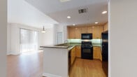 This single-floor residence offers a cohesive and functional layout designed for comfortable everyday living. The kitchen serves as a central highlight, outfitted with warm honey-toned wood cabinetry, green-hued granite countertops, and a full suite of black appliances including a gas range, microwave, and refrigerator. Recessed lighting illuminates the space, while a peninsula with a granite countertop and integrated sink provides additional workspace and a natural transition into the open living area. The living room is generously proportioned, featuring light wood-look flooring, clean white walls, and an arched passageway connecting it to the kitchen. Natural light filters in through vertical blinds along an exterior window wall.

The space includes two bathrooms, both featuring granite-topped vanities with light wood cabinetry and large mirrors. One bathroom includes a tub-shower combination with sliding glass doors, while the other functions as a half bath. Both feature earthy tile flooring. The bedrooms are finished with plush carpet and neutral walls, each offering access to a walk-in closet equipped with multiple hanging rods and shelving. The overall aesthetic is clean, neutral, and move-in ready.