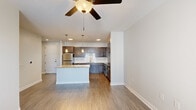 This thoughtfully designed single-floor residence offers a seamless blend of modern style and functional living. The open-concept layout centers around a standout kitchen, which features rich dark-toned shaker cabinetry, granite countertops, a subway tile backsplash, and a full suite of stainless steel appliances including a refrigerator, range, microwave, and dishwasher. A large kitchen island with a granite surface provides generous prep space and serves as a natural gathering point. Pendant lighting and recessed ceiling lights illuminate the kitchen, while a ceiling fan anchors the adjacent living area, which flows seamlessly from the kitchen. Wood-look plank flooring runs throughout the main living spaces, lending warmth and continuity to the open floor plan. A hallway connects the living areas to the private quarters, where bedrooms are finished with plush carpet, ceiling fans, and natural light from windows with blinds. The primary bedroom includes access to a spacious walk-in closet with built-in shelving. A bathroom with granite countertops and clean, neutral finishes completes the layout. Throughout the residence, crisp white walls, clean lines, and consistent finishes create a cohesive, move-in-ready environment.