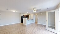 Located at 200 Arbor Pl in New Albany, Indiana, this single-floor residence offers a clean, modern design with a cohesive neutral color palette and light hardwood-style flooring carried consistently throughout every room. The open-concept living and kitchen area forms the heart of the home, where a central peninsula with granite countertops and bar seating serves as both a functional workspace and a natural gathering point. Dark espresso cabinetry provides rich contrast against the light countertops, and black appliances — including a range, microwave, and refrigerator — complete the kitchen. A dedicated pantry with wire shelving sits conveniently adjacent to the cooking area, offering generous storage. The living area is bright and airy, illuminated by ceiling fan light fixtures and recessed lighting, creating an inviting atmosphere. Bedrooms are well-proportioned, each featuring ceiling fans and hardwood-style flooring, with one bedroom enjoying a window that draws in natural light. A spacious walk-in closet outfitted with wire shelving and hanging rods provides ample storage. The bathroom includes a full tub-shower combination with clean white surround finishes. Throughout the space, white trim and neutral walls contribute to a fresh, move-in-ready aesthetic.