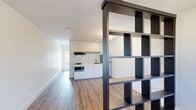 Located at 645 W Pullman Rd in Moscow, Idaho, this thoughtfully designed studio offers a single-floor open layout that makes efficient use of its intimate footprint. The main living area features warm wood-look flooring and crisp white walls, creating a bright and welcoming atmosphere. A striking black open-grid shelving unit serves as a creative room divider, subtly separating the living space from the kitchenette while maintaining an airy, connected feel throughout. The kitchenette is anchored by white cabinetry, a subway tile backsplash, a butcher block-style countertop, and a range with an overhead vent hood, delivering both style and functionality. Natural light filters in through well-placed windows, enhancing the clean, modern aesthetic. The bathroom continues the contemporary design language with floor-to-ceiling large-format white subway tile, dark hexagonal floor tile, matte black fixtures, a walk-in shower, and a navy vanity with a white countertop — a bold, elegant combination. A shared outdoor deck runs along the exterior of the building, offering open views of the surrounding landscape under wide Idaho skies, providing an inviting outdoor retreat. This unit presents a cohesive, modern living experience with carefully curated finishes throughout.