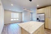 Located in Parker, Colorado, this well-appointed 2-bedroom, 2-bathroom residence showcases a clean, contemporary design with cohesive finishes throughout. The open-concept kitchen and living area serves as the heart of the home, centered around a striking kitchen island topped with a veined quartz countertop. Light wood-tone cabinetry pairs with stainless steel appliances — including a side-by-side refrigerator, built-in microwave, and range — while a textured herringbone tile backsplash adds a refined detail. Sleek pendant lighting illuminates the island, and recessed lighting brightens the entire living space. Wood-look plank flooring flows seamlessly through every room, lending warmth and visual continuity. Natural light enters through multiple windows fitted with roller shades. The primary bedroom connects directly to an en-suite bathroom featuring a glass-enclosed walk-in shower with herringbone tile and a window for natural light. The second bathroom offers a full soaking tub and shower combo with matching tile work and a wood-toned vanity. Both bedrooms are well-proportioned, with dedicated closets providing ample storage. The unit also includes a private exterior entry door, adding convenience and a sense of independence to this modern Parker residence.
