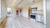 Located at 1312 Church St in Lynchburg, Virginia, this single-floor unit offers a thoughtfully arranged layout spread across multiple rooms. Light wood-style luxury vinyl plank flooring runs throughout, creating a cohesive and clean aesthetic from room to room.

The kitchen is efficiently designed with white shaker-style cabinetry, granite-look countertops, and a full suite of stainless steel appliances including an electric range, over-the-range microwave, dishwasher, and a French door refrigerator. Natural light filters in through windows, complementing the bright, neutral color palette.

The main living area features a ceiling fan with light fixture, a wall-mounted mini-split HVAC unit for year-round climate control, and a welcoming entry framed by a bold red glass-panel door with exposed white-painted brick accents. The open sightlines between the living space and kitchen enhance the sense of openness throughout.

Additional rooms, finished in warm cream tones, offer flexible use potential. The bathroom includes a walk-in shower, a vanity with white countertop and blue-grey cabinetry, classic white tile flooring, and recessed wall niches for storage. Barn-style black hardware on interior doors adds a modern rustic touch throughout the space.