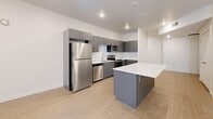 This well-appointed 3-bedroom, 2-bathroom single-story home offers a thoughtfully designed layout with a clean, modern aesthetic. The open-concept living, dining, and kitchen area serves as the heart of the home, featuring light wood-style flooring that flows seamlessly throughout the common spaces. The kitchen is a standout, equipped with stainless steel appliances including a refrigerator, range, microwave, and dishwasher, complemented by gray cabinetry, white quartz countertops, a subway tile backsplash, and a central island ideal for dining or meal prep. The living area opens to the outdoors through glass-paneled French doors, bringing in natural light and providing outdoor access. Each of the three bedrooms is carpeted for comfort, with the bedrooms featuring ceiling fans and windows for natural ventilation. The primary bedroom includes a double-door closet and is served by a private en-suite bathroom with a glass-enclosed walk-in shower, gray vanity, and wood-look flooring. A second full bathroom offers a tub-shower combination with the same modern gray vanity finish. Additional highlights include four closets for ample storage, an in-unit laundry area, and a connecting hallway that ties the floor plan together efficiently.