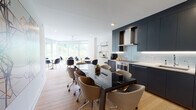 Located at Riverview Circle in North Bergen, NJ, this single-floor space presents a thoughtfully designed, contemporary work environment. The open-plan kitchen and dining area serves as a central hub, featuring sleek navy cabinetry, stainless steel appliances including double wall ovens and a professional refrigerator, light tile backsplash, and a wall-mounted range hood. A large black conference table with ergonomic chairs anchors this space, while floor-to-ceiling windows along one wall flood the area with natural light and offer lush green outdoor views.

Multiple dedicated conference rooms provide varied meeting settings. One features a marble-top table with black mesh chairs and a wall-mounted display, while another offers a warm walnut table with upholstered seating and its own screen. A third, larger meeting room with greenery-facing windows accommodates additional seating. A comfortable lounge area with modern upholstered chairs and a glass coffee table offers an informal gathering space.

Two well-appointed bathrooms complete the layout—one featuring a glass-enclosed walk-in shower and another with a full bathtub—both finished with large-format travertine-style tiles, floating wood vanities, and illuminated mirrors, conveying a clean, refined aesthetic throughout.