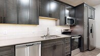 This 530 square foot apartment offers a thoughtful blend of comfort and efficiency. The open-concept layout creates a sense of spaciousness, with the kitchen seamlessly integrated into the living area. The modern kitchen boasts dark wood cabinetry, stainless steel appliances, and a generously sized island that doubles as a dining space. Pendant lighting adds a touch of sophistication.

The living area is bright and airy, with large windows providing ample natural light and city views. Wood-look flooring throughout enhances the contemporary aesthetic. The 90 square foot bedroom, while compact, features plush carpeting and corner windows for added light and dimension. A closet provides essential storage space.

The bathroom is efficiently designed with a combined tub and shower, modern fixtures, and wood-look flooring that complements the rest of the apartment. Throughout the space, recessed lighting and neutral tones create a clean, modern ambiance. This apartment maximizes every square foot, offering a comfortable living space in a urban setting.