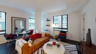 Located at 1250 Half St in Washington, DC's vibrant Navy Yard neighborhood, this modern single-floor residence offers a thoughtfully designed layout with clean lines and contemporary finishes throughout. The living area is bright and welcoming, featuring large black-framed windows that invite abundant natural light and offer views of the surrounding cityscape. The space accommodates a comfortable seating arrangement alongside a dedicated dining area, creating a versatile environment for both relaxing and entertaining.

The kitchen is outfitted with light wood cabinetry, a subway tile backsplash, white quartz countertops, and a full suite of stainless steel appliances, including a French door refrigerator, range, and over-the-range microwave. A large window adjacent to the kitchen brings in additional natural light.

The residence includes multiple bedrooms, each finished with neutral-toned walls, dark hardwood flooring, and windows overlooking the neighborhood. The bedrooms offer generous proportions with ample closet space. Two bathrooms serve the home — one featuring a glass-enclosed walk-in shower with white tile surround and dark wood vanity, and a second with a full soaking tub and tiled shower combination. Both bathrooms maintain a clean, modern aesthetic consistent with the rest of the residence.