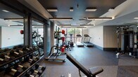 Located at 372 Fourth Ave in the heart of downtown San Diego, this well-appointed fitness center delivers a comprehensive workout environment designed for both functionality and comfort. The space is anchored by a striking design contrast: dark, matte-painted ceilings fitted with sleek linear LED lighting panels set against clean white walls, creating a modern and energizing atmosphere.

The gym is divided into distinct functional zones. A dedicated free weights and strength training area features a rack of dumbbells, a multi-functional cable machine, and a bench press station, all positioned alongside floor-to-ceiling mirrors that enhance the sense of space. A separate cardio zone lines the perimeter near large windows, housing treadmills, stationary bikes with integrated digital screens, and additional cardio equipment — all benefiting from natural light and views of the surrounding streetscape.

An open training zone with rubber flooring and a clearly marked workout circle provides ample space for functional fitness and stretching. Well-organized equipment racks hold a colorful assortment of kettlebells and medicine balls, keeping the space tidy and accessible. Dual stainless steel water fountains and a prominent wall clock add practical amenities for users. The durable rubber flooring throughout ensures safety and noise reduction across the entire space.