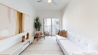 Located at 2828 Santa Monica Blvd in Santa Monica, California, this single-floor unit showcases a clean, contemporary design with a bright, open-concept layout and light hardwood flooring throughout. The kitchen is well-appointed with stainless steel appliances including a gas range, microwave, and refrigerator, complemented by flat-front cabinetry in a soft gray-white finish, open shelving, a subway tile backsplash, and a undermount sink with a matte black faucet. A dedicated dining area flows naturally from the kitchen, offering space for a round table and seating. The living area is airy and inviting, featuring a ceiling fan, a sliding glass door that opens to a private balcony, and generous wall space for art display. The bedroom is cozy and well-lit by a window, maintaining the unit's consistent neutral palette. The bathroom features blue ceramic tile surrounding a soaking tub and shower combination, a floating gray vanity with a white countertop, a round mirror with a black frame, and tile flooring. Throughout the unit, the white walls and natural light create a calm, cohesive ambiance well-suited to the Southern California lifestyle.