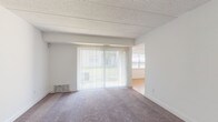 This single-floor residence offers a clean, functional layout with a neutral color palette throughout, creating a bright and welcoming atmosphere. The expansive living room is finished with plush carpeting and features a large sliding glass door fitted with vertical blinds, allowing abundant natural light and providing a view of the greenery outside. The open layout connects seamlessly to adjacent areas, offering a versatile and airy feel.

The kitchen is a standout feature, equipped with white cabinetry, dark granite countertops, and white appliances including a range and over-the-range microwave. A peninsula with matching granite extends the counter space and adds a natural separation between the kitchen and the adjacent area, which is finished with warm hardwood-style flooring.

The bedrooms are generously sized, each featuring soft carpeting, ample natural light from windows with blinds, and white walls that lend a clean and neutral backdrop. One bedroom notably includes dual closets with bifold doors, providing excellent storage capacity.

The bathroom is updated with dark wood-look vinyl plank flooring, white cabinetry with dark countertops, and a full tub-shower combination. The space is practical and well-appointed throughout, making it a comfortable and move-in ready residence.