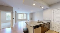 This thoughtfully designed 1-bedroom, 2-bathroom residence offers a functional and modern single-floor layout. The open-concept kitchen and living area serve as the heart of the home, anchored by a granite-topped peninsula with an undermount sink and stainless steel appliances, including a refrigerator, range, and microwave. Rich dark-stained cabinetry and a classic tile backsplash add depth and character to the kitchen. Light hardwood flooring flows throughout the main living areas, complementing the neutral wall tones and recessed lighting. The living room is bright and welcoming, featuring a wide triple-panel window that frames lush green tree views and fills the space with natural light. A track light fixture overhead adds a modern touch. The primary bedroom offers plush carpeting, generous wall space, and windows with outdoor views, creating a comfortable retreat. The primary bathroom is well-equipped with a granite-topped dual vanity, dark wood cabinetry, a large mirror, and access to a walk-in closet outfitted with wire shelving. A second bathroom provides additional convenience. Throughout the space, clean lines, consistent finishes, and an abundance of natural light create a cohesive and inviting atmosphere.