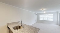 This single-floor unit offers a clean, contemporary layout designed for comfortable everyday living. The kitchen is equipped with rich dark-wood cabinetry, granite countertops, and a full suite of stainless steel appliances, including a refrigerator, electric range, over-the-range microwave, and a stainless steel sink — all set atop durable hardwood-style flooring. The kitchen opens to a bright and spacious living area featuring plush wall-to-wall carpeting, crisp white walls with crown molding, and a wall-mounted mini-split HVAC unit for personalized climate control. A window allows natural light to fill the space, creating an open and airy ambiance. The bedroom area continues the neutral color palette with soft carpeting and multiple white paneled doors leading to a double closet and additional storage. The full bathroom is neatly finished with granite-topped dark wood vanity cabinetry, a framed mirror, elegant brushed nickel fixtures, and a combination shower and soaking tub. Hardwood-style flooring extends through the bathroom, tying the space together with a cohesive aesthetic. Overall, this unit delivers a functional, move-in-ready environment with consistent, quality finishes throughout.