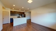 This single-floor unit showcases a clean, contemporary design with a thoughtful open-concept layout. The combined kitchen and living area forms the heart of the space, where rich hardwood-style flooring runs continuously underfoot, complemented by neutral white walls and recessed lighting that keeps the area bright and welcoming.

The kitchen is well-appointed with dark espresso cabinetry extending to the upper walls for generous storage, light-toned quartz-style countertops, and a full suite of stainless and black stainless appliances, including a French door refrigerator, electric range, and over-the-range microwave. A peninsula with seating potential separates the kitchen from the open living area, enhancing both functionality and flow.

Two carpeted bedrooms offer a quieter, softer finish and each feature large windows that bring in natural light along with views of the surrounding neighborhood. Sliding closet doors provide accessible built-in storage in each room.

The full bathroom is finished consistently with the rest of the unit, featuring dark vanity cabinetry, a white countertop with an integrated sink, a tub-shower combination, and hardwood-style flooring, creating a cohesive and practical space throughout.
