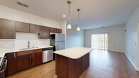 This thoughtfully designed 1-bedroom, 1-bathroom residence delivers a practical and comfortable living experience across a single floor. The open-concept kitchen and living area form the heart of the home, featuring rich dark wood cabinetry, white countertops, and a full suite of stainless steel appliances including a refrigerator, dishwasher, electric range, and built-in microwave. A central kitchen island with pendant lighting above provides additional prep space and a natural gathering point. Wood-look flooring flows throughout the main living areas, while the spacious living room benefits from abundant natural light and direct outdoor access through sliding glass doors fitted with vertical blinds. The generously sized bedroom offers plush carpeting, a large window with outdoor views, and a walk-in closet equipped with wire shelving systems for organized storage. The full bathroom features matching dark wood cabinetry, a white countertop vanity, a large mirror, and wood-look flooring. A dedicated in-unit laundry room houses a full-size washer and dryer with overhead wire shelving. A hallway connects all areas of the residence, completing this efficiently arranged and move-in-ready home.