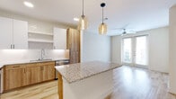 This well-designed one-bedroom, one-bathroom unit offers a thoughtful layout across a single floor, making efficient use of every square foot. The open-concept kitchen and living area serves as the heart of the home, where light wood-tone flooring, soft neutral walls, and a ceiling fan create a bright and airy atmosphere. Natural light flows in through French doors that open to an outdoor view, further enhancing the sense of openness.

The kitchen is a standout feature, outfitted with a full suite of stainless steel appliances including a refrigerator with ice maker, range, microwave, and dishwasher. Warm wood lower cabinetry pairs with crisp white upper cabinets, while a subway tile backsplash and granite countertops — extending across a generous kitchen island — add a polished, modern touch. Pendant lighting above the island completes the look. A stacked in-unit washer and dryer is conveniently tucked just off the main living area.

The bedroom is carpeted for comfort, featuring a window with outdoor views that brings in ample natural light. The bathroom is clean and functional, with a tub-shower, built-in storage cabinetry, and direct access to a dedicated walk-in closet equipped with shelving and hanging space — offering practical organization throughout.