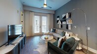 Located at 1050 Slater Rd in Durham, NC, this thoughtfully designed single-floor residence offers a cohesive blend of modern aesthetics and practical functionality. The open-concept kitchen is outfitted with stainless steel appliances including a French door refrigerator, gas range, and built-in microwave, complemented by light wood cabinetry with matte black hardware and a white quartz island with an undermount sink and pendant lighting overhead. Wood-look flooring runs throughout the unit, creating a warm and consistent visual flow. The living room features French doors that open to a balcony, allowing natural light to pour in, while a ceiling fan and bold accent wall add character to the space. Two well-proportioned bedrooms offer windows with natural light and ample closet space, including a spacious walk-in closet with wire shelving. The bathroom is finished with a wood-tone vanity, white quartz countertop, large framed mirror, and a tub-shower combination with marble-style tile surround. A dedicated laundry closet with a front-load washer provides added in-unit convenience. A stylish barn door detail near the hallway adds a distinctive architectural touch to this well-appointed home.