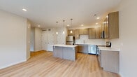 Located at 1915 S Mattis Ave in Champaign, IL, this well-designed 2-bedroom, 1-bathroom residence offers a thoughtfully laid-out single-floor plan with contemporary finishes throughout. The open-concept kitchen and living area serves as the heart of the home, anchored by a central island with a crisp white countertop and stylish pendant lighting overhead. The kitchen is fully equipped with stainless steel appliances — including a refrigerator, dishwasher, microwave, and range — complemented by warm-toned shaker-style cabinetry that extends to the ceiling for generous storage. Light hardwood flooring runs throughout the main living areas, enhancing the bright and airy atmosphere created by recessed lighting. The living area opens to natural light through large windows and a door with outdoor access, offering pleasant views of surrounding greenery. Both bedrooms feature soft carpeting and ample natural light, with the second bedroom providing an outward-facing window view. The bathroom includes a vanity with storage, a glass-enclosed shower, and consistent wood-look flooring. Wire shelving in the bathroom adds practical storage. The neutral color palette and clean architectural lines give the entire space a modern, move-in-ready appeal.