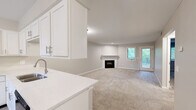 Located at 200 Lake Forest Blvd in Kalamazoo, Michigan, this two-bedroom, one-bathroom residence offers a well-organized single-floor layout designed for comfortable everyday living. The open-concept kitchen and living room serve as the heart of the home, where plush neutral carpet in the living area transitions to light wood-style flooring in the kitchen. A fireplace with a clean white mantel anchors the living room, complemented by recessed lighting and a window that brings in natural light and greenery views. The kitchen is well-appointed with crisp white shaker-style cabinetry, light stone countertops, black appliances including a range with overhead microwave and a dishwasher, and a window that enhances the bright, airy feel. Both bedrooms are carpeted and generously sized, each offering closet storage — the primary bedroom features a built-in shelving closet system. The shared bathroom is a standout, boasting a dual-sink vanity with white cabinetry, a wide mirror, recessed lighting, and wood-style flooring. A hallway connects the private areas of the home efficiently. Neutral tones throughout create a cohesive, move-in ready aesthetic.