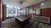 Located at 183 E Main St in the heart of downtown Rochester, NY, this single-floor amenity space blends historic architectural character with contemporary design. The entry lobby sets a sophisticated tone with its ornate marble medallion floor inlay, checkered tile border, intricate decorative metalwork, and rich crimson accent walls. A stylish console table, globe-shaped accent lighting, and curated artwork add to the refined atmosphere.

The billiards lounge is a standout feature, centered around a full-size pool table beneath an eye-catching industrial-style chandelier with exposed Edison bulbs. Floor-to-ceiling windows flood the space with natural light and offer views of the surrounding cityscape, while high bistro tables and red accent chairs complete the social setting. A decorative wall installation of varied door panels adds an artistic, eclectic touch.

A private dining area accommodates a large party around a dark wood table with bold red upholstered chairs. Cascading globe pendant fixtures in brushed gold provide warm, ambient lighting, complemented by a living green wall element and generous window views.

The lounge area features generous wraparound sectional seating in warm terracotta and rust tones, layered over textured patterned carpet. Pendant lighting and recessed fixtures create an inviting, relaxed atmosphere ideal for gathering and socializing throughout the space.