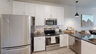This single-story unit in Austin, Texas, offers a thoughtfully designed open-concept layout that seamlessly connects the kitchen, dining, and living areas. The kitchen is a standout feature, equipped with stainless steel appliances, dark granite countertops, a peninsula with undermount sink and pendant lighting, and crisp white shaker cabinetry extending to the ceiling for ample storage. A tile backsplash and light wood-style flooring complete the polished look.

The living area is bright and welcoming, benefiting from multiple large windows and a glass-paned door that opens to a private outdoor space, filling the room with natural light and greenery views. A ceiling fan adds comfort overhead.

The bedroom is a calm retreat with plush carpeting, multiple windows dressed with sheer curtains and blinds, and a ceiling fan. It connects directly to a well-appointed full bathroom featuring dark granite countertops, white cabinetry, and a large mirror. Adjacent to the bathroom is a dedicated walk-in closet with built-in shelving and hanging rods, providing generous storage. The overall palette of soft neutrals and white tones gives the space a clean, contemporary ambiance throughout.