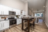 This well-designed two-story home offers four bedrooms and three bathrooms across a generously sized layout. The main floor features an open-concept kitchen and living area, where white shaker-style cabinetry, granite countertops, subway tile backsplash, and stainless steel appliances create a clean, modern kitchen. The adjoining living room is bright and welcoming, with large black-framed windows that invite natural light and outdoor views. Light hardwood flooring flows throughout the main level, lending warmth and continuity to the space. A stylish sliding barn door leads to the dedicated laundry room, which includes a stacked washer and dryer alongside wire shelving for added storage. The upper floor houses the primary bedroom, which is comfortably proportioned and includes a walk-in closet outfitted with wire shelving and carpet flooring. The bathrooms are finished with granite-topped white vanities and glass-enclosed walk-in showers. Additional bedrooms feature plush carpet and neutral tones, offering flexible living arrangements. A utility room with HVAC infrastructure rounds out the lower level. Throughout, the home maintains a consistent palette of soft neutrals, clean trim work, and thoughtful finishes that contribute to a cohesive, move-in-ready atmosphere.